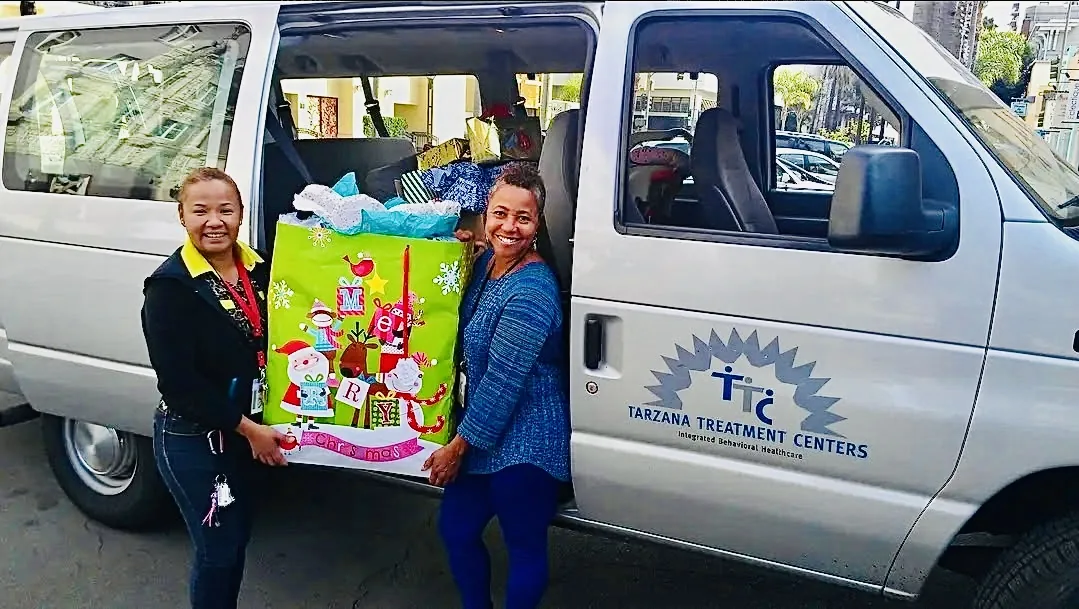 Two H.O.P.E. volunteers holding a large Christmas gift bag beside a community van