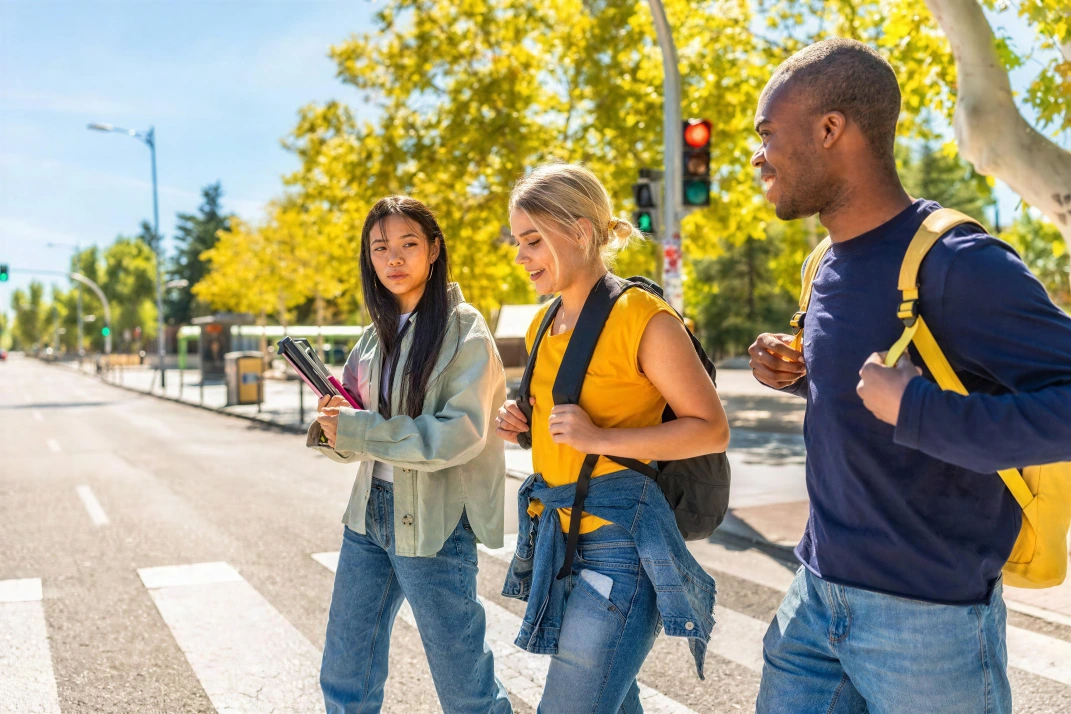 Three young adults with backpacks crossing a city street together